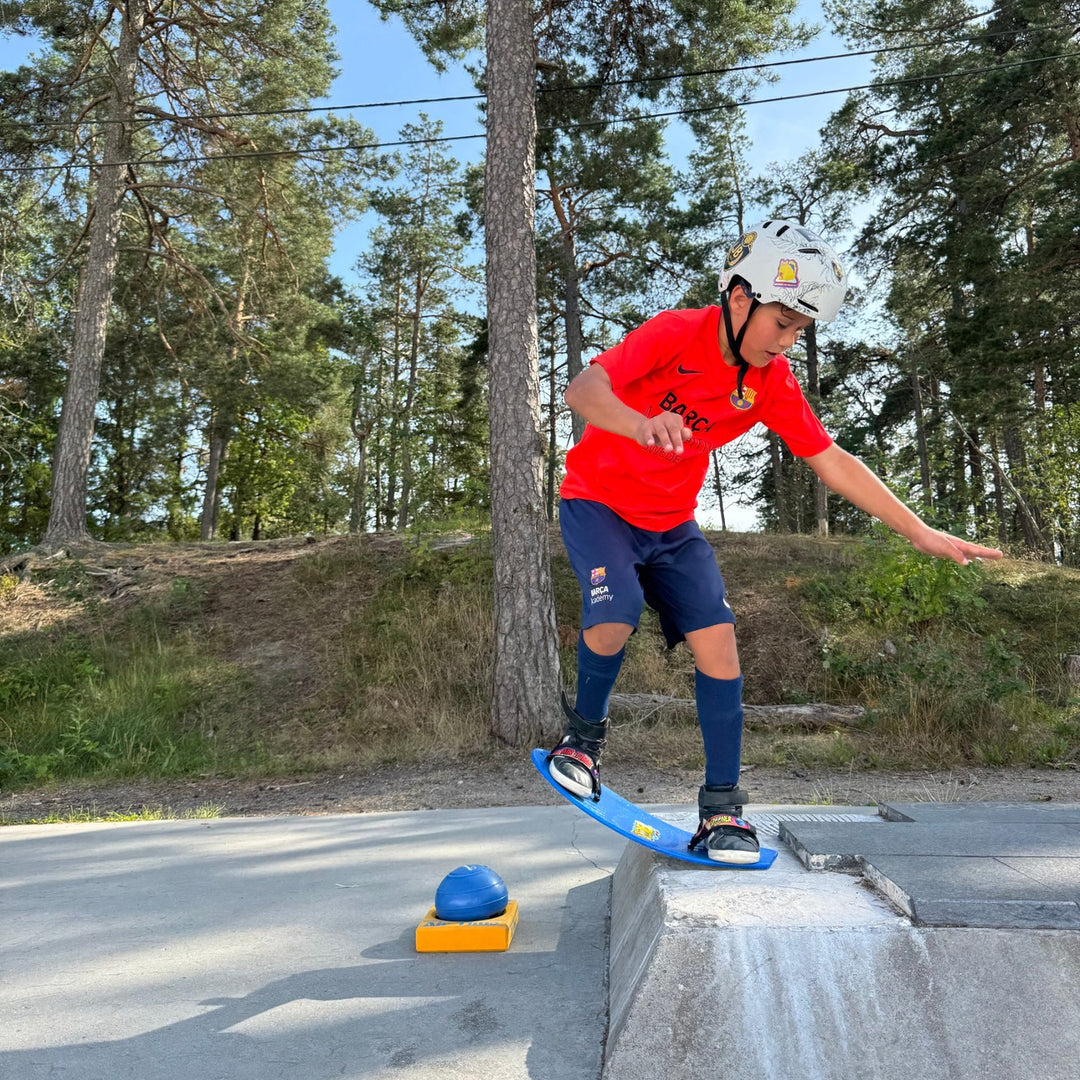 Boy riding a blue Spooner board with AirPro footstraps along a skatepark ledge, AirBall on its base beside him
